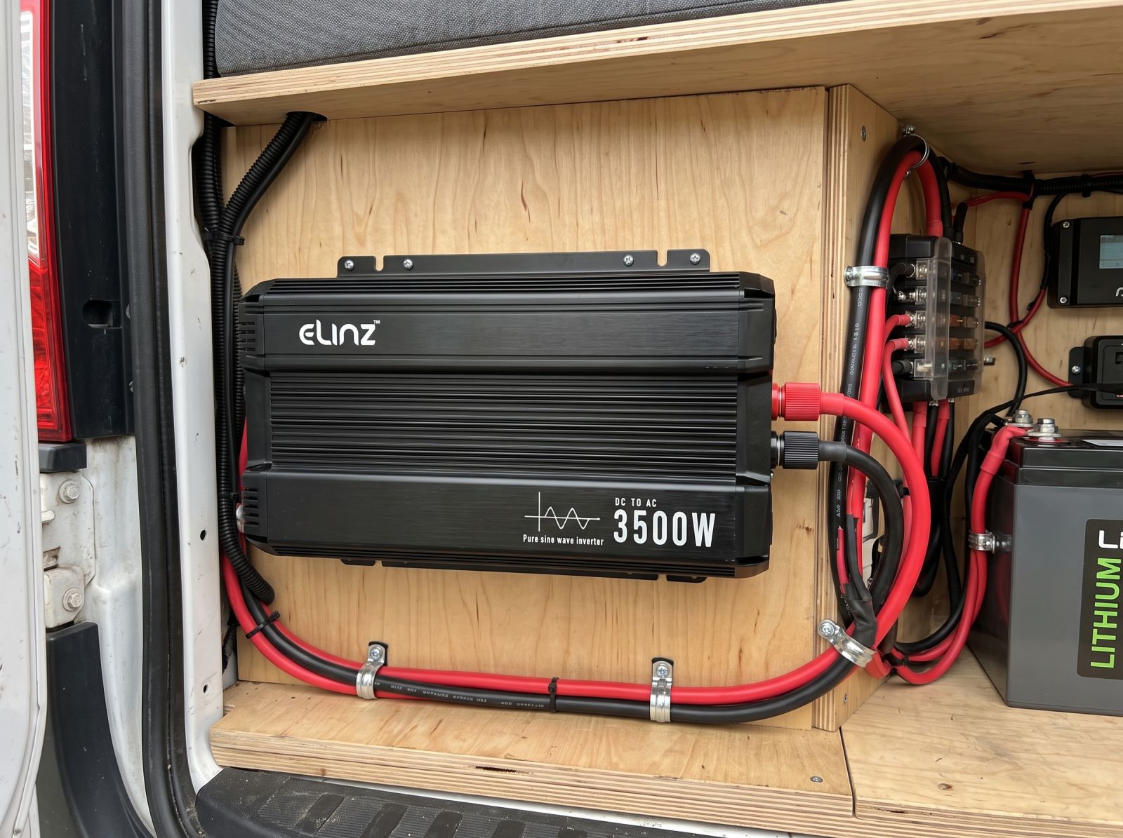 Close-up of a 3500W pure sine wave inverter with red and black power cables installed inside a camper van.