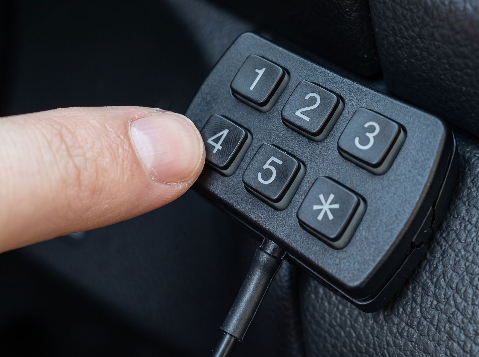 Close-up of a black car immobiliser keypad with numbered buttons being operated by a finger.