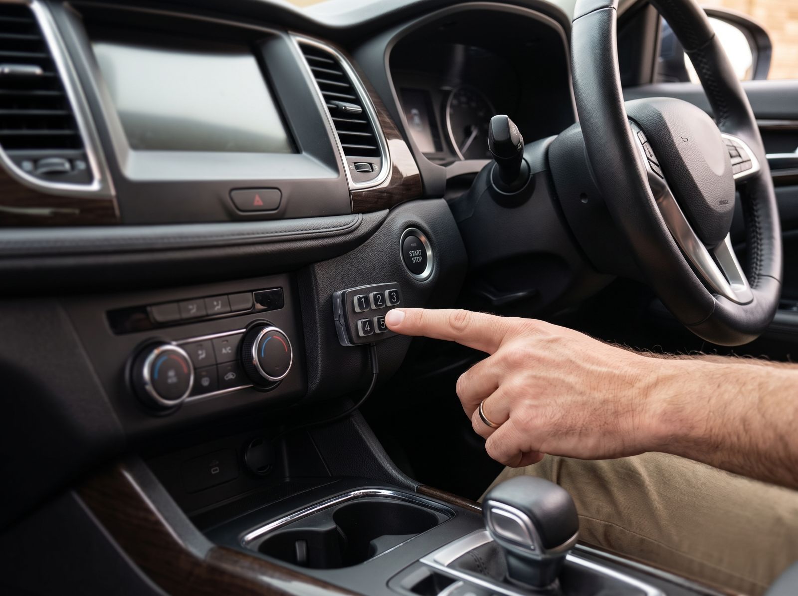 Car interior with a push-button ignition and security keypad being operated beside the steering wheel.