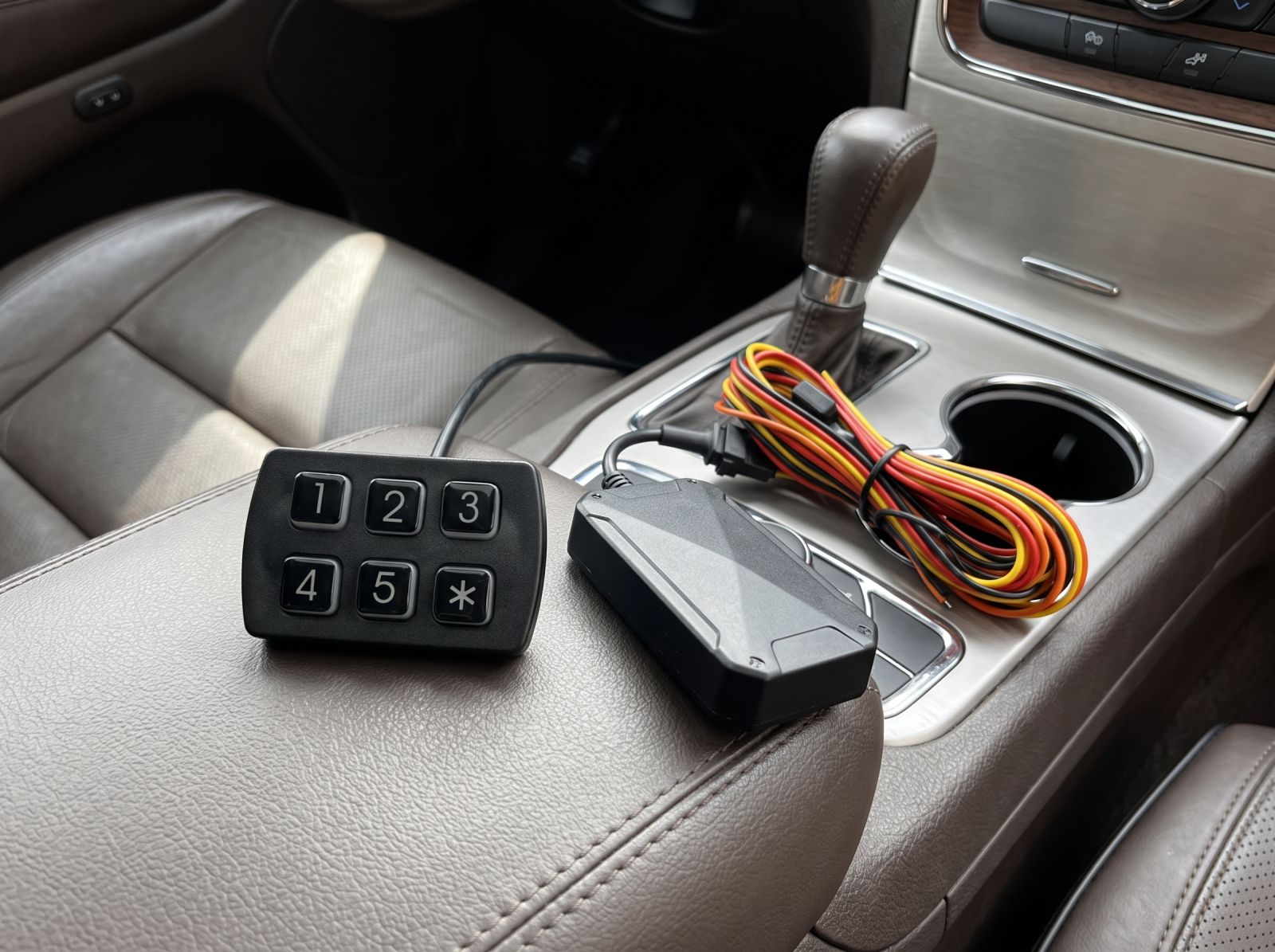 Engine keypad immobiliser kit with keypad controller, control module and wiring harness displayed on a car centre console before installation.